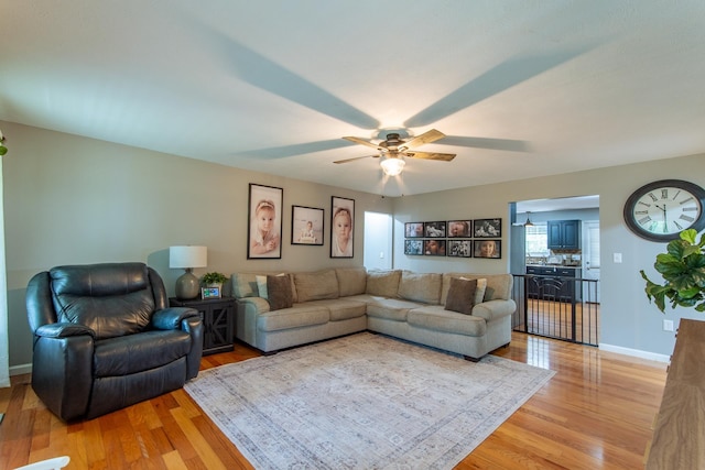 living room with a ceiling fan, baseboards, and light wood-style flooring