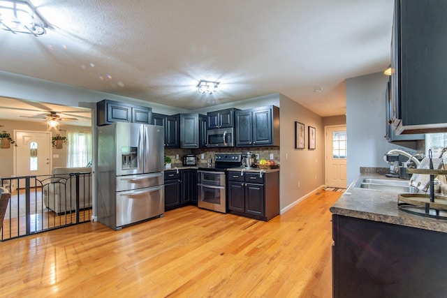 kitchen with appliances with stainless steel finishes, a sink, light wood-style flooring, a ceiling fan, and decorative backsplash