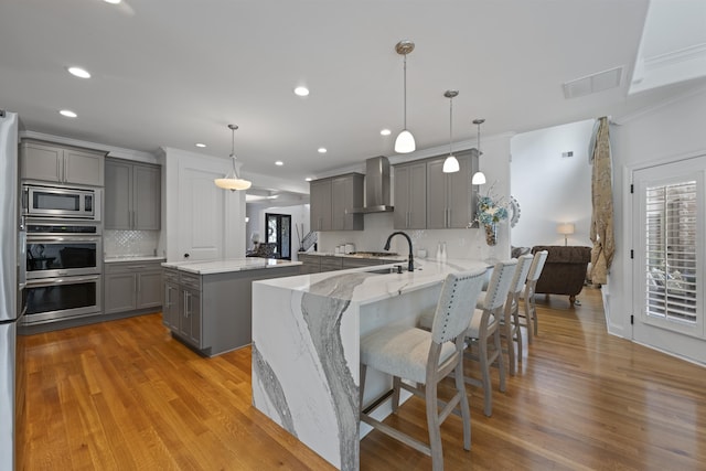kitchen featuring gray cabinets, tasteful backsplash, a peninsula, stainless steel appliances, and wall chimney exhaust hood