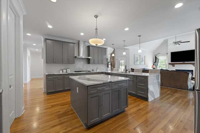kitchen featuring gray cabinets, wall chimney exhaust hood, a peninsula, open floor plan, and gas stovetop