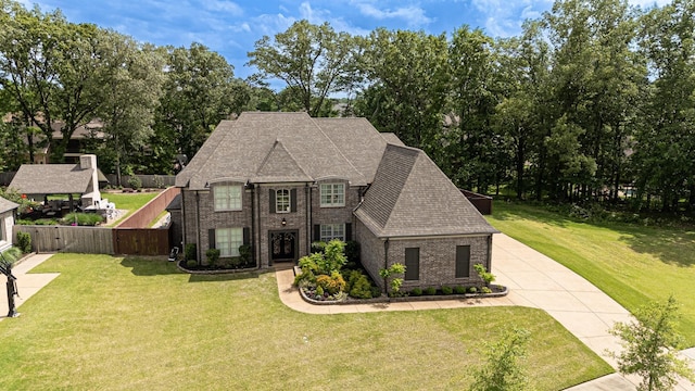 french country home with concrete driveway, brick siding, and a front lawn