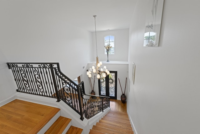 stairs featuring baseboards, wood finished floors, and a notable chandelier