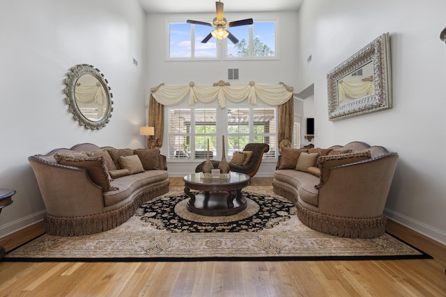 living room featuring visible vents, baseboards, ceiling fan, and a wealth of natural light
