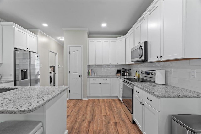 kitchen featuring ornamental molding, washer / dryer, white cabinets, light wood finished floors, and appliances with stainless steel finishes