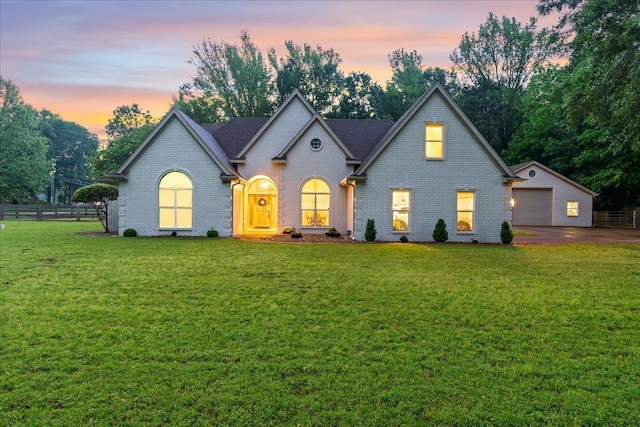 view of front facade with brick siding, a garage, a lawn, and fence