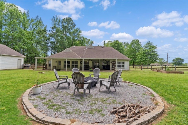 back of property featuring a lawn, a ceiling fan, a garden, and a fire pit