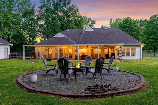 back of house at dusk with a lawn, a fire pit, fence, and a patio area