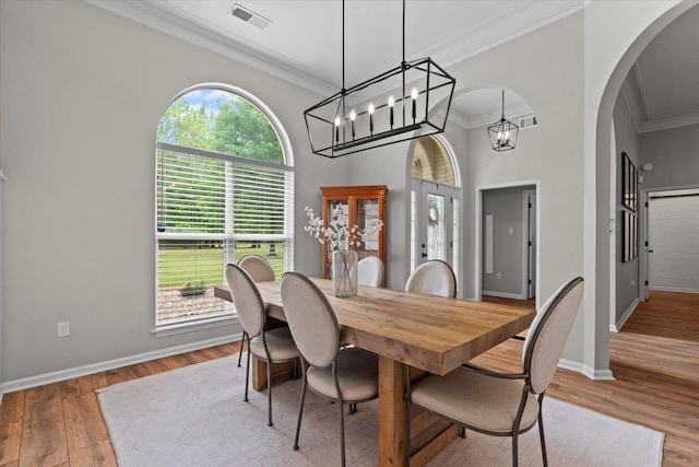 dining room featuring visible vents, ornamental molding, wood finished floors, baseboards, and arched walkways