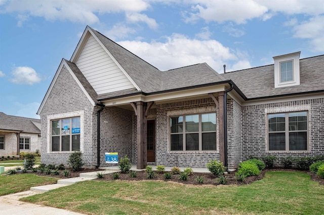 view of front of home featuring brick siding, a front yard, and roof with shingles