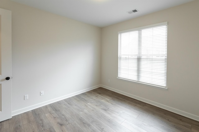 spare room featuring visible vents, baseboards, plenty of natural light, and wood finished floors