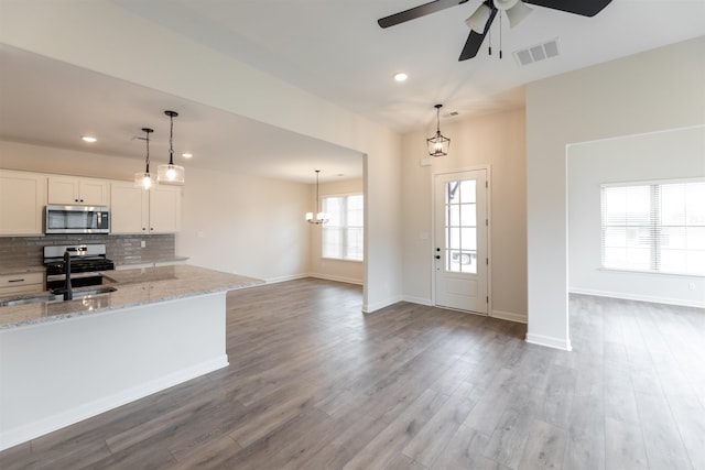 kitchen with white cabinets, light stone countertops, appliances with stainless steel finishes, a sink, and ceiling fan with notable chandelier