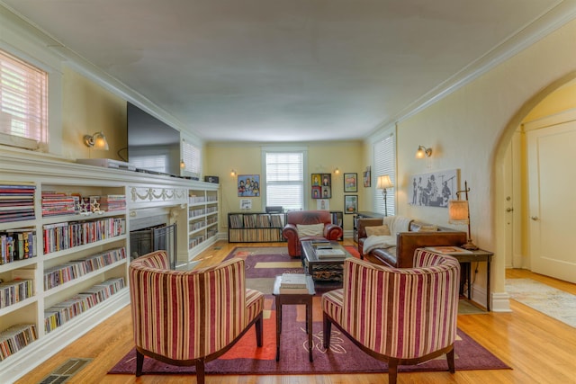 living area with crown molding, arched walkways, a fireplace, and wood finished floors