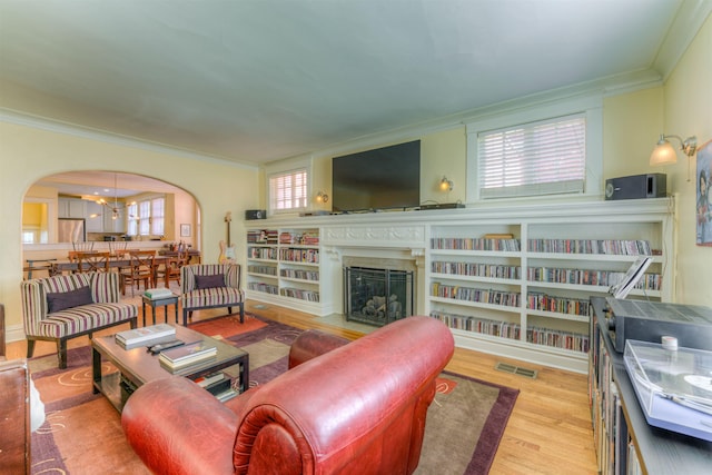 living area with crown molding, arched walkways, a fireplace with flush hearth, wood finished floors, and visible vents