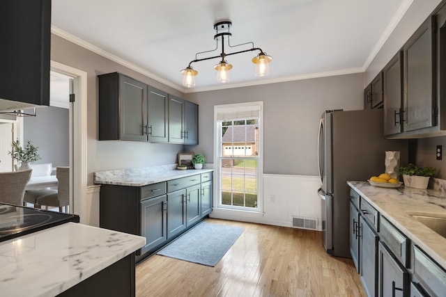 kitchen with light stone counters, light wood finished floors, a wainscoted wall, visible vents, and ornamental molding