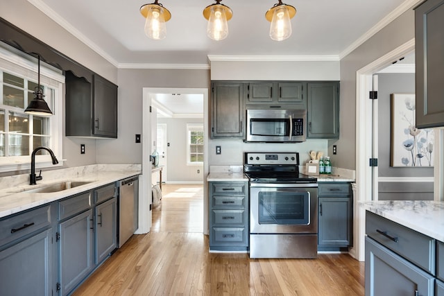 kitchen with hanging light fixtures, a sink, light wood-style flooring, stainless steel appliances, and ornamental molding