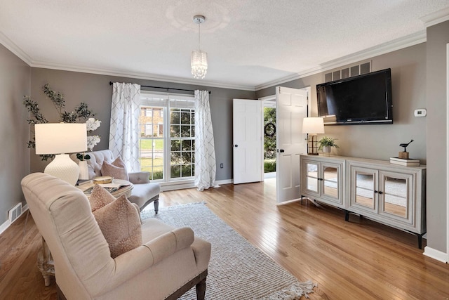 living room featuring a textured ceiling, visible vents, wood finished floors, baseboards, and ornamental molding