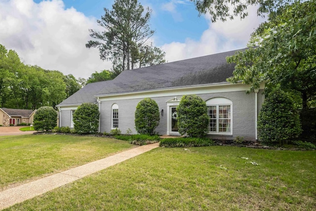 view of front of home with brick siding, a shingled roof, and a front lawn