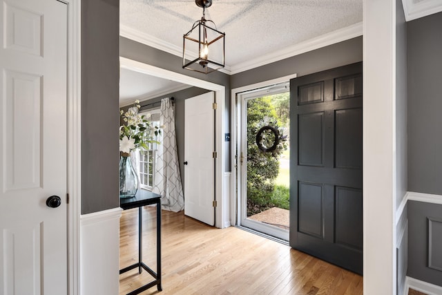 foyer featuring crown molding, a textured ceiling, a chandelier, and light wood-style flooring