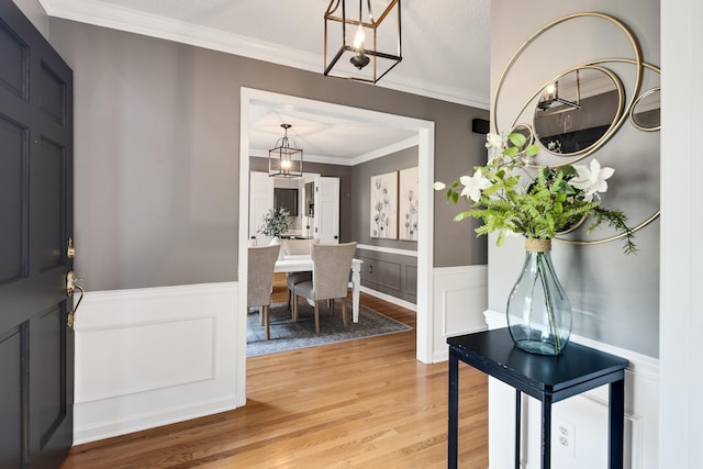 foyer featuring an inviting chandelier, wainscoting, a decorative wall, light wood-style flooring, and ornamental molding