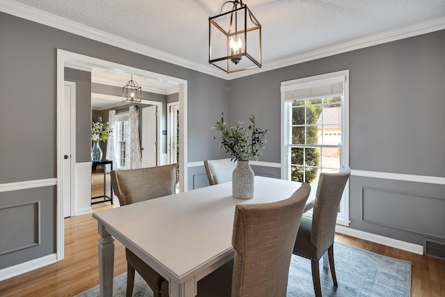 dining area featuring crown molding, a notable chandelier, wainscoting, a decorative wall, and wood finished floors