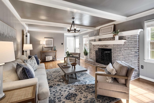 living room with a notable chandelier, a brick fireplace, light wood-type flooring, beamed ceiling, and ornamental molding