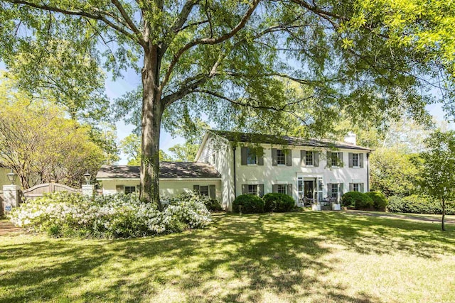 colonial inspired home featuring a chimney, stucco siding, and a front lawn