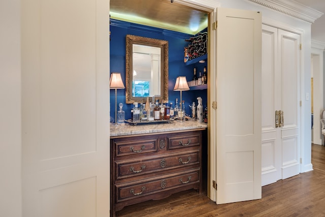 bar with dark wood finished floors, ornamental molding, and a bar