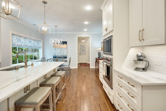 kitchen featuring appliances with stainless steel finishes, a sink, a chandelier, ornamental molding, and a breakfast bar