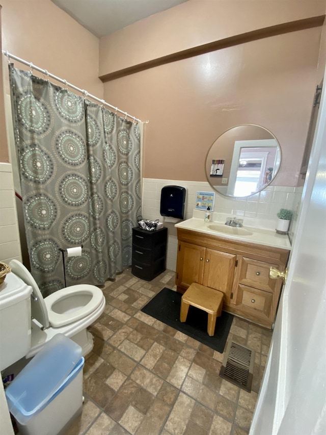bathroom with visible vents, tile walls, a wainscoted wall, vanity, and toilet