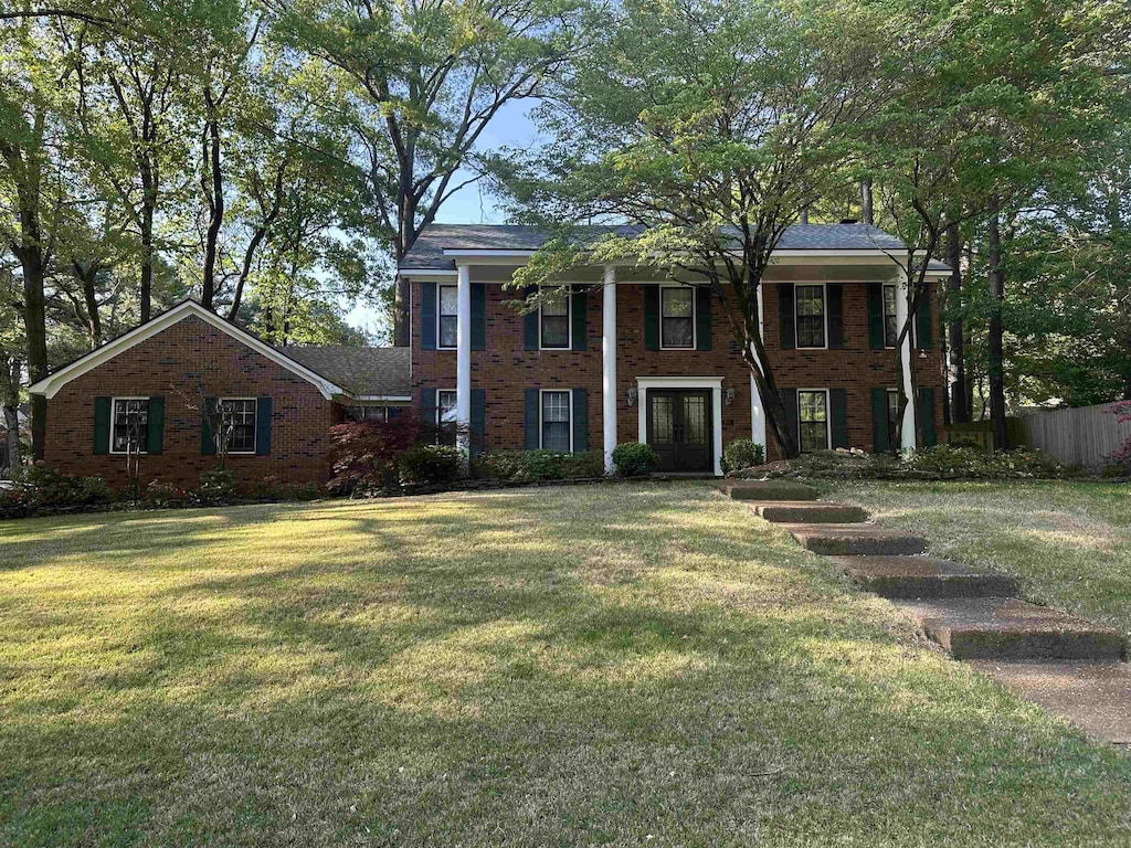 greek revival house featuring brick siding, a front lawn, fence, and french doors