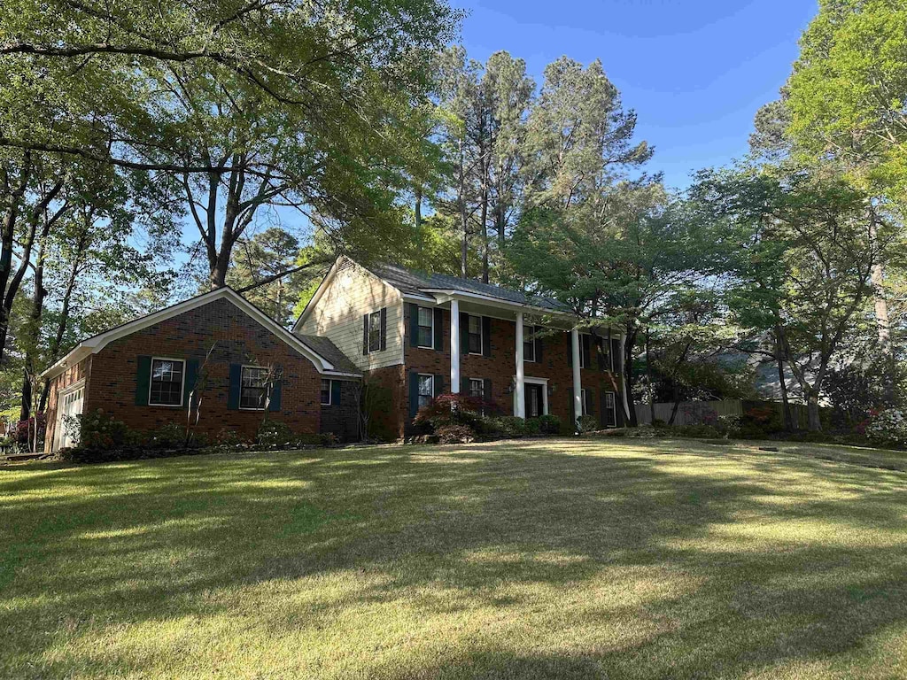 greek revival inspired property with an attached garage, a front yard, and brick siding