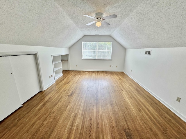additional living space with visible vents, built in features, lofted ceiling, wood finished floors, and a textured ceiling