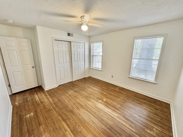 unfurnished bedroom with visible vents, baseboards, wood finished floors, and multiple windows