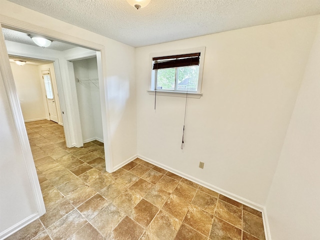 unfurnished room with a textured ceiling, baseboards, and stone finish flooring