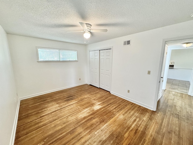 unfurnished bedroom featuring visible vents, baseboards, wood finished floors, and a closet
