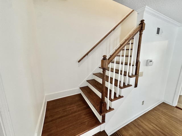 staircase with baseboards, ornamental molding, a textured ceiling, and wood finished floors