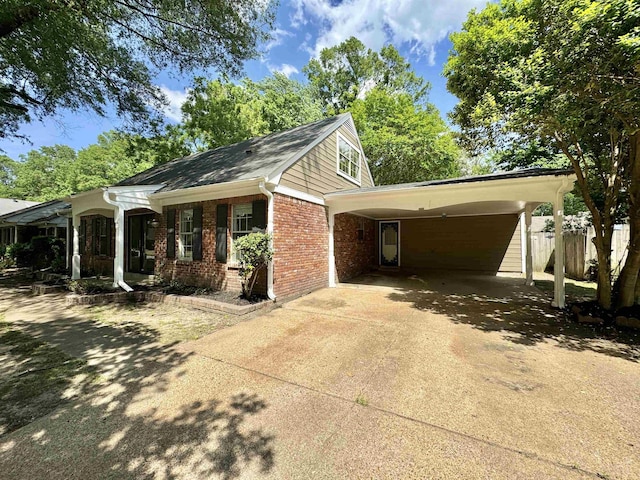 view of side of home featuring fence, a carport, driveway, and brick siding