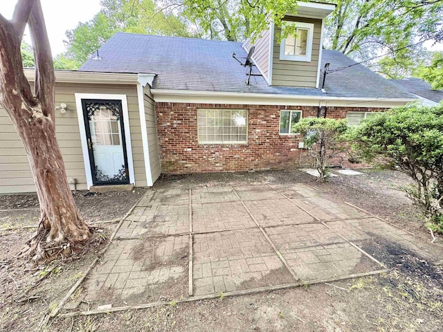 back of property featuring a patio, a shingled roof, and brick siding