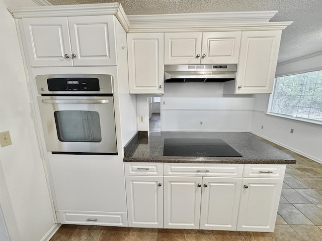 kitchen featuring a textured ceiling, black electric cooktop, white cabinets, under cabinet range hood, and oven