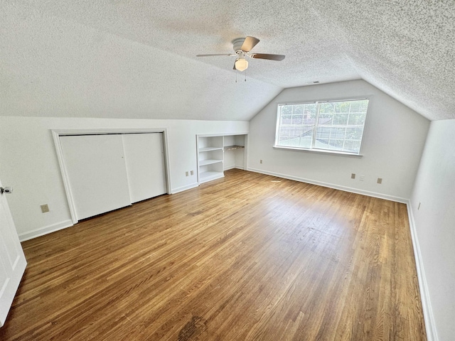 bonus room featuring a textured ceiling, built in features, and baseboards