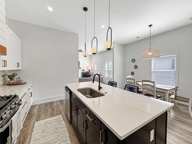 kitchen featuring pendant lighting, an island with sink, white cabinetry, a sink, and appliances with stainless steel finishes