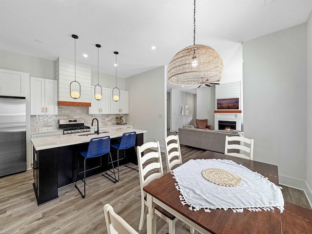 dining room with recessed lighting, baseboards, light wood finished floors, and a warm lit fireplace