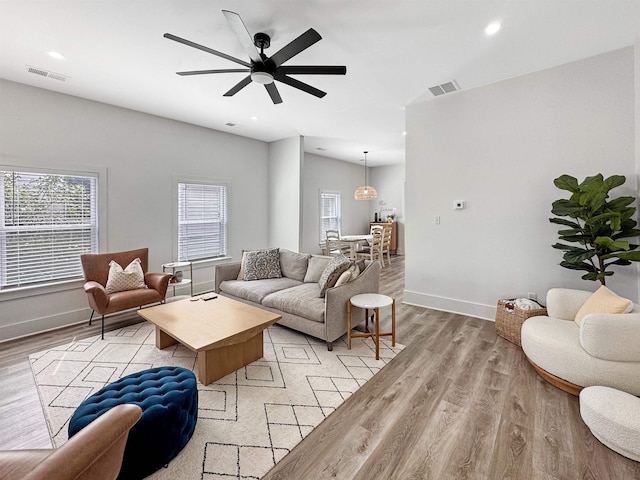 living area with visible vents, light wood finished floors, ceiling fan, and baseboards