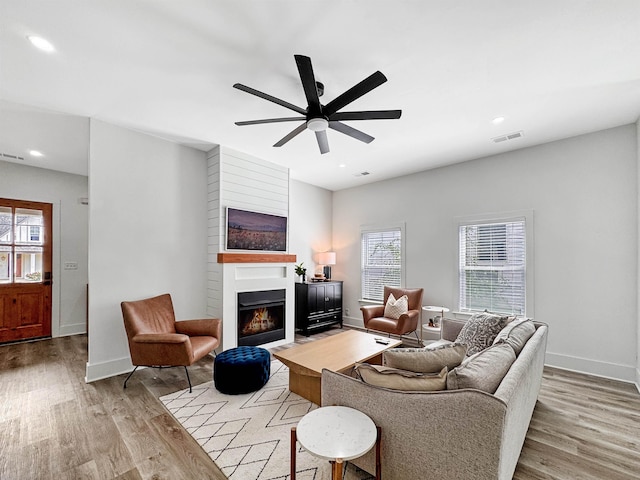living area featuring a warm lit fireplace, a healthy amount of sunlight, and light wood-style floors