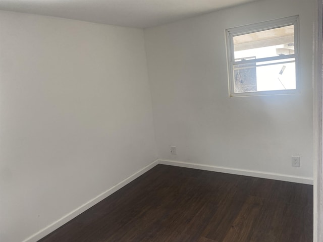 unfurnished room featuring baseboards and dark wood-type flooring