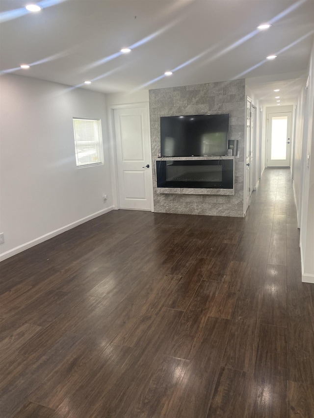 unfurnished living room with baseboards, a glass covered fireplace, and dark wood-style floors