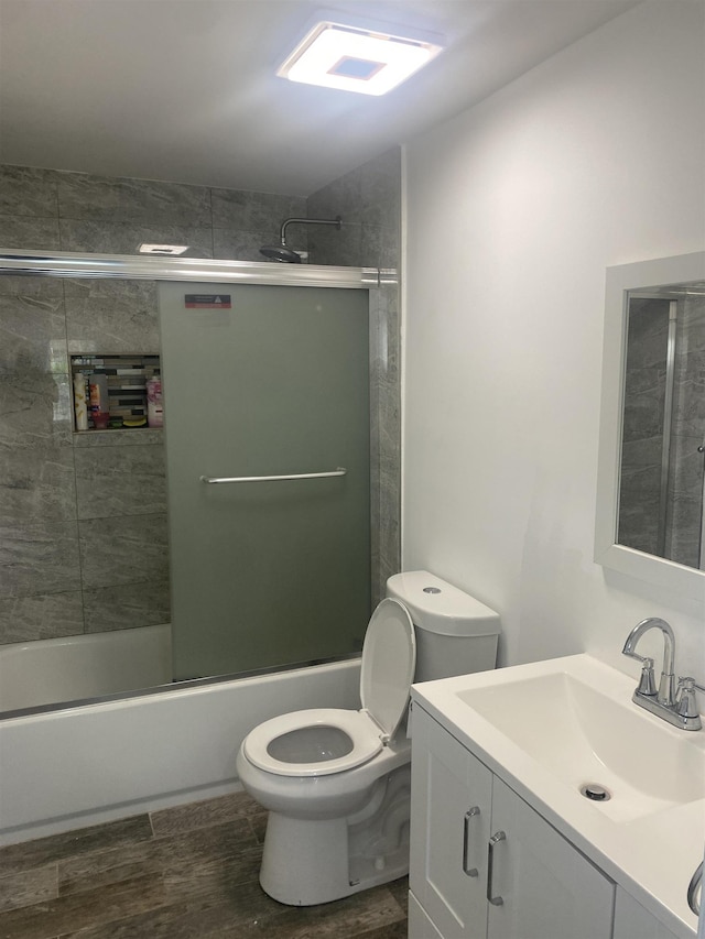 full bathroom featuring toilet, wood finished floors, bath / shower combo with glass door, and vanity