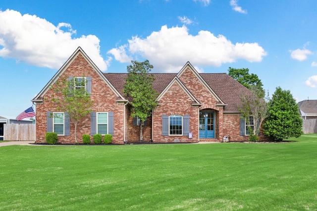 view of front of property with fence, roof with shingles, brick siding, and a front yard
