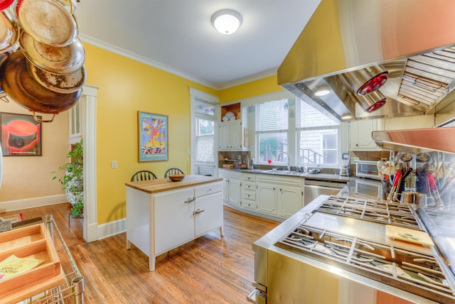 kitchen with crown molding, a sink, a healthy amount of sunlight, and wall chimney range hood