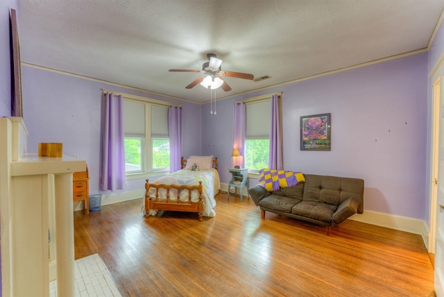 bedroom featuring ceiling fan, visible vents, crown molding, wood finished floors, and baseboards